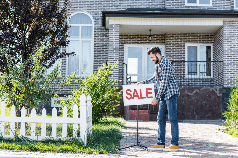 Man putting up for sale sign in front of house
