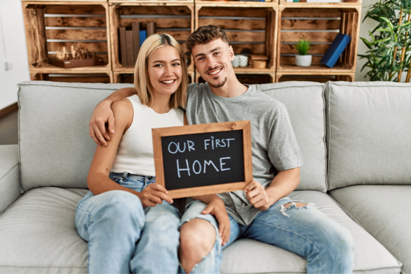 Young smiling couple holding a sign that says "our first home"